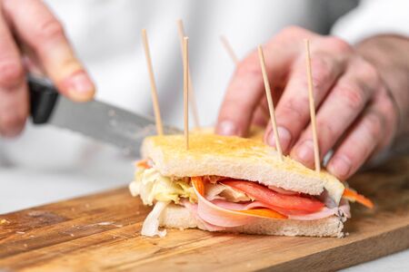 Chef finalizes the sandwich with ham and salad on the wooden board.