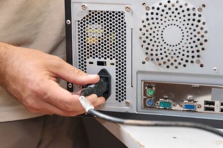 Man hand inserts power cord into a computer.