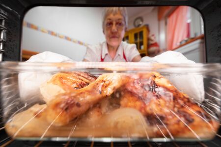 Senior woman taking roasted chicken from the oven, viewed from the interior.の写真素材
