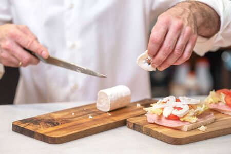 Chef making sandwich in rustic style with ham fresh vegetables and goat cheese. Delicious food.