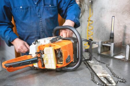 Mechanic repairing a chainsaw. Man repairing a chainsaw in workbench.