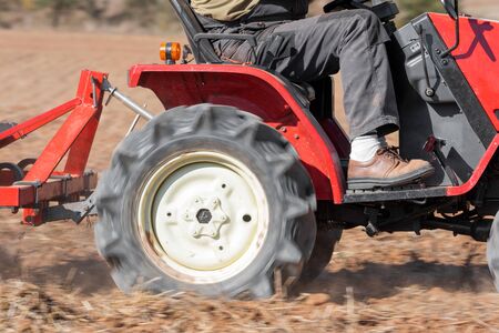 Red Tractor With Plough Plowing Field Soil Close Up View.の写真素材