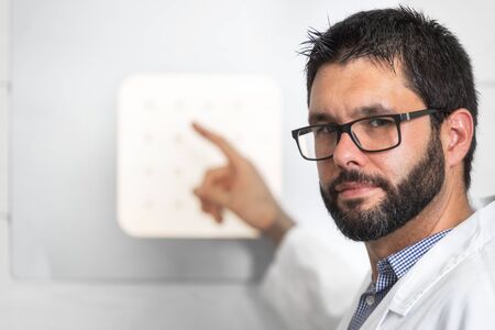 Doctor Optician With Letter Chart Conducting An Eye Test Check.
