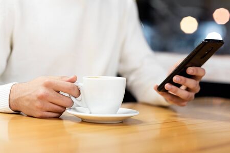 Handsome young caucasian man sitting at cafe using mobile phone and having coffee. Caucasian male...