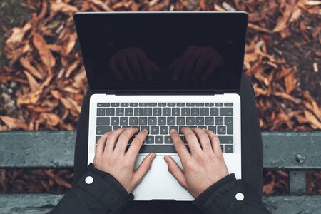 Top view, of young man sitting on park bench on autumn with laptop. Student using computer outdoors.の写真素材