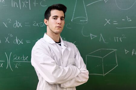 College student in laboratory class. College student with white coat, standing in front of chalkboard.の写真素材
