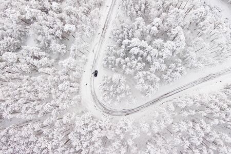 Car on road in winter trough a forest covered with snow. Aerial photography of a road in wintertime trough a forest covered in snow. High mountain pass.の写真素材