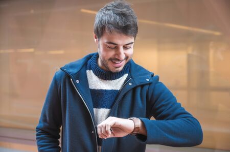 Young happy man portrait Looking At His Watch. Urban Background.の写真素材