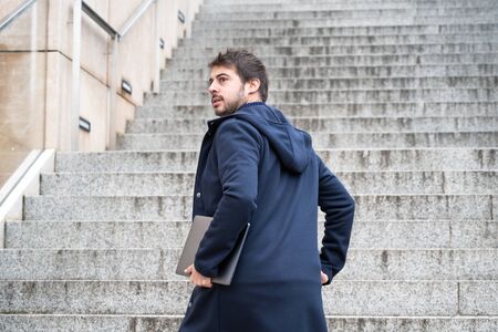 Young man Holding Computer Laptop Walking Up Stairs outdoor.