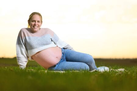 Beautiful pregnant woman lying on the park at sunset. Outdoors pregnant portrait.の写真素材