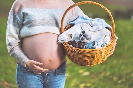 Pregnant woman expecting a baby, posing outdoors with a wicker basket with clothes for her newborn.の写真素材