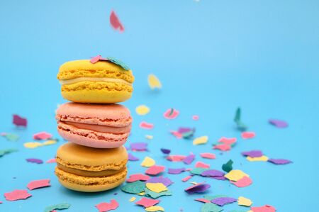 Colorful macarons on trendy pastel blue paper with confetti. tasty pink, yellow and brown macaroons...