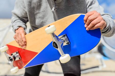 Close up of unrecognizable young man holding longboard or skateboard in the park.