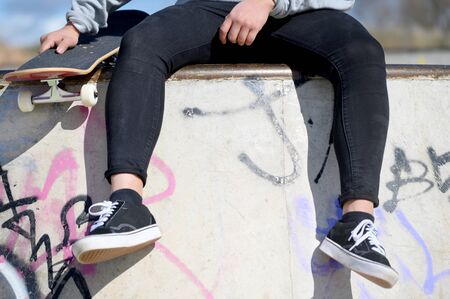 Close up of unrecognizable young man seated with skateboard in the park.の写真素材
