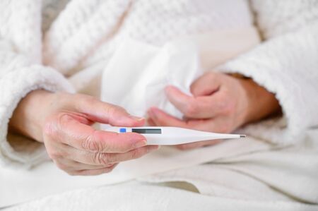 Coronavirus. Sick senior woman holding tissue and thermometer sit on bed, upset old mature woman...