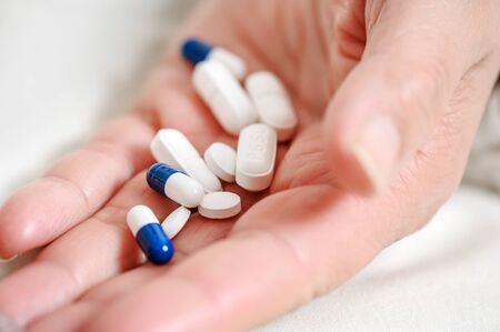 medicine, healthcare and people concept - close up of senior woman hand with pills.