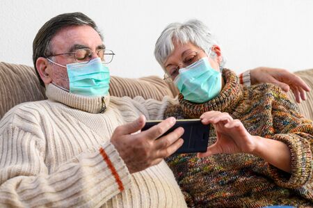 Coronavirus. Stay at home, lifestyle. Cheerful Elderly couple sitting on a sofa on a quarantine at...
