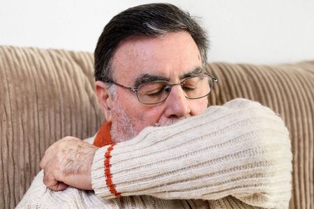 Elderly people sneezing, coughing into her sleeve or elbow to prevent spread Covid-19. Corona virus, sick senior man has flu, sneezing covering nose, mouth with his arm.の写真素材