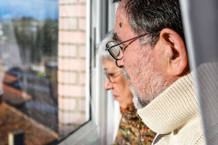 Concept of coronavirus quarantine and social distancing. Senior couple, at home looking through the...