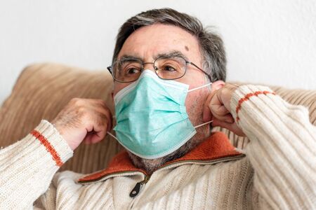 Elderly man putting a medical mask on his face to protect himself from coronavirus pandemic.