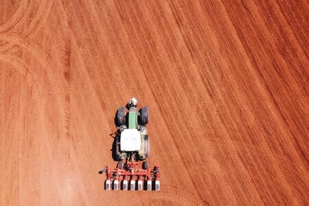 Farmer seeding, sowing crops at field with tractor. Sowing is the process of planting seeds in the ground as part of agricultural activities.の写真素材
