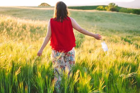 Unrecognizable woman walking outdoors throwing away her mask. Young happy girl removing protective mask. End of pandemic coronavirus concept. Meadow landscape, Pollen allergy at spring.の写真素材