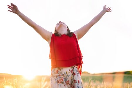 Young woman arms raised up to sky, celebrating freedom. Positive emotions feeling life perception success, peace of mind concept. Free Happy girl in summer meadow enjoying sunset in nature.の写真素材