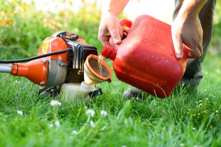 Gardener refueling brush cutter close up. Gardening tools maintenance. Lawn care with brush cutters.
