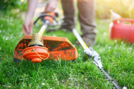 Gardener preparing grass trimmer on lawn in garden outdoors.