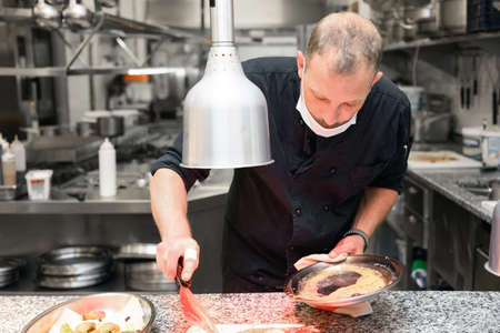 Chef in uniform cooking in a commercial kitchen. Male cook standing by kitchen counter preparing...