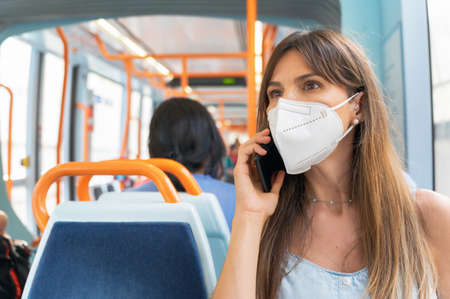 Woman wearing face mask talking on the phone onboard train