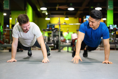 Two young men doing high planks in gym.