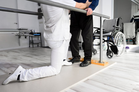Physiotherapist helping disabled Caucasian senior man to walk with parallel bars in rehabilitation center.の写真素材