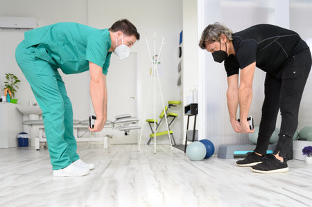 Physiotherapist showing movements of rehabilitation therapy for male patient.