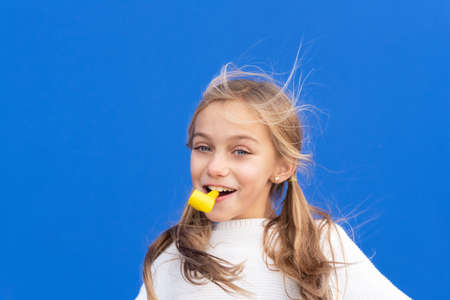Studio portrait of a happy, smiling young girl celebrating birthday party, holding party blower in...