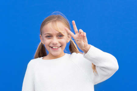Young beautiful blond girl wearing casual sweater over blue background smiling looking to the camera...