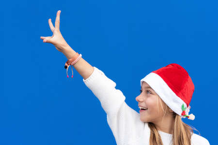 Joyful Young girl in Santa hat gesturing on blue background.の写真素材