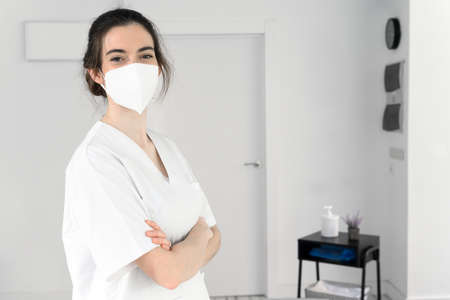 Friendly female physiotherapist posing in modern clinic wearing protective face mask during pandemic
