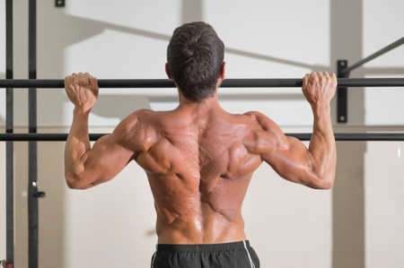 Athlete doing pull-ups at the gym. Handsome man doing functional training.