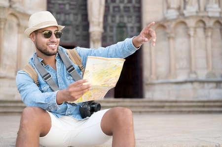 Handsome tourist man look at map while pointing finger in the direction of destination. Travel concept. Trip, backpacker tourist.の写真素材
