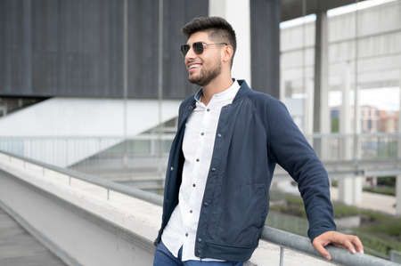 Portrait of a young confident smiling man standing beside modern building looking into the distanceの写真素材