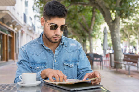 Young traveller man sitting in a cafe terrace and planning her trip with map and laptopの写真素材