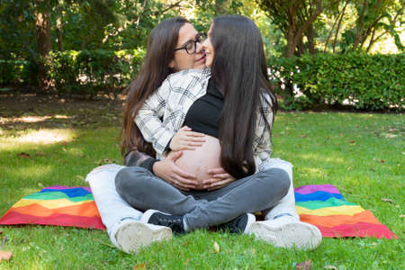 Portrait of affectionate pregnant lesbian couple with rainbow flag, relaxed at the park. Two happy girlfriends. Free same-sex love. Homosexual relationship. LGBT Community Prideの写真素材