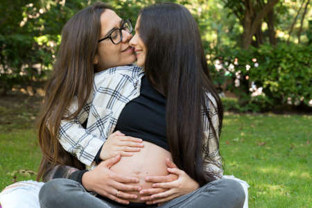 Portrait of affectionate pregnant lesbian couple relaxed at the park. Two happy girlfriends. Free same-sex love. Homosexual relationship. LGBT Community Prideの写真素材