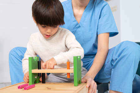 cute kid with disability playing with developing toys while is being helped by physiotherapist in rehabilitation hospital.の写真素材