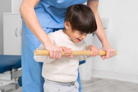 Physiotherapist and kid walking in rehabilitation center. Doctor supports a children with cerebral palsy during physiotherapy treatment.の写真素材