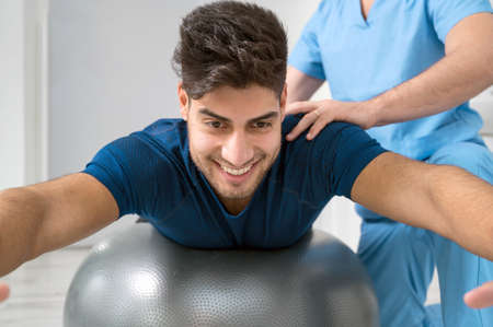 Physiotherapist helps handsome young patient with pilates exercises.の写真素材
