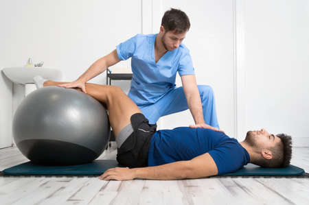 Physiotherapist helps handsome young patient with pilates exercises.の写真素材