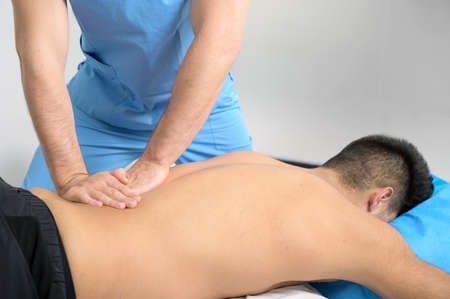 Physiotherapist massaging the back of a young athlete in the sports rehabilitation clinic.の写真素材