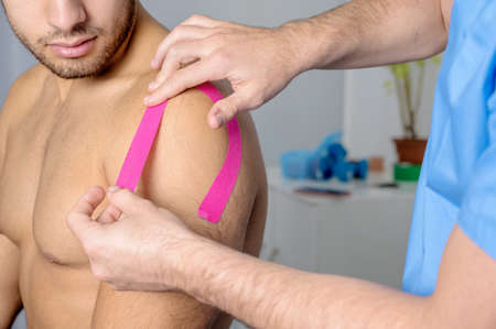 Physical therapist applying kinesio tape on male patient shoulder. Kinesiology, physical therapy, rehabilitation concept. close upの写真素材